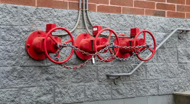 Red fire department connection valves on a wall secured with chains and a padlock.