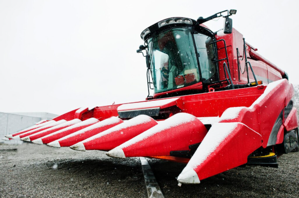 Red combine harvester with corn header parked on gravel, modern agricultural harvesting machine in winter conditions.
