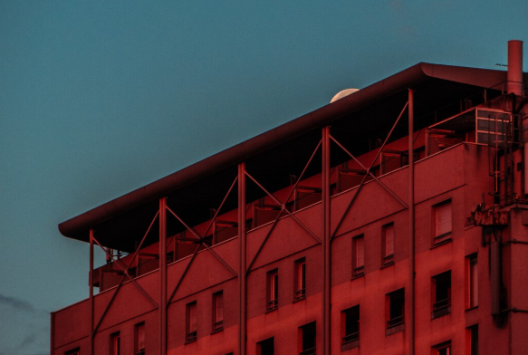 Red industrial building with modern architectural lines illuminated at dusk against a blue evening sky.
