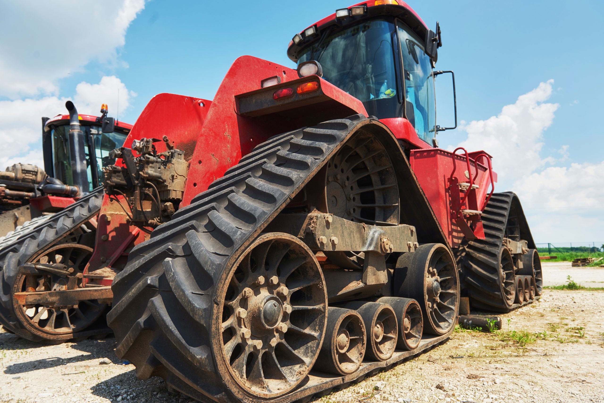 Large red tracked construction machine paarked on a farm under a blue sky.